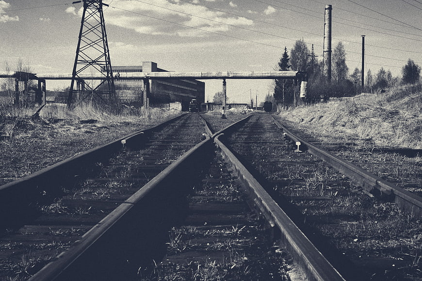 Black and white railway tracks leading to industrial landscape