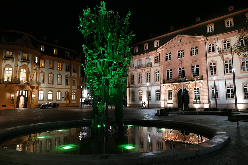 Green illuminated fountain sculpture in European square at night