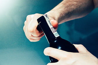 Close-up of hands opening a dark wine bottle