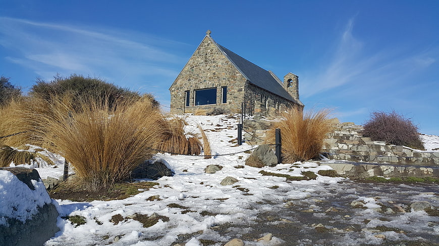 Stone Church on Snowy Hillside Under Blue Sky