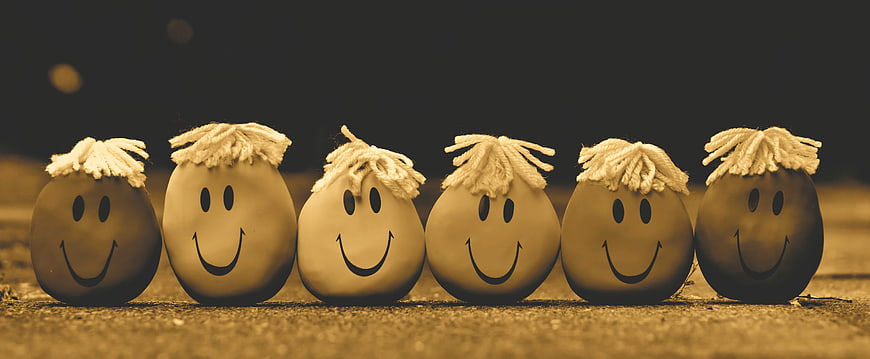 Row of six smiling anti-stress balls with yarn hair on a textured surface