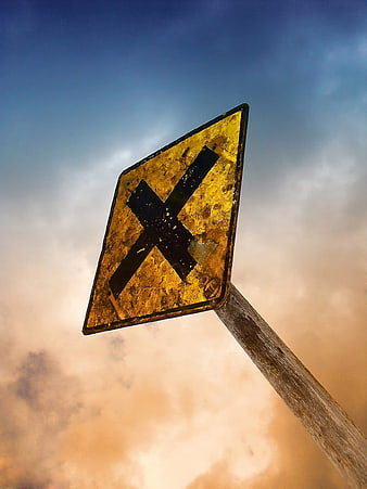 Rusty railroad crossing sign against dramatic sunset sky