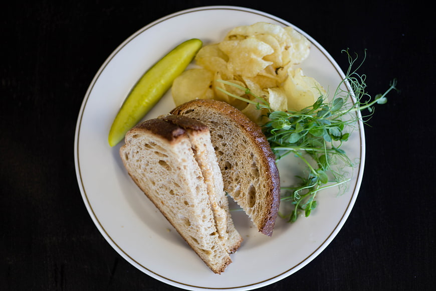 Sliced bread, chips, and pickle on a white plate