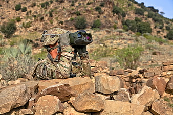 Soldier Using Binoculars Behind Rock Wall In Arid Landscape