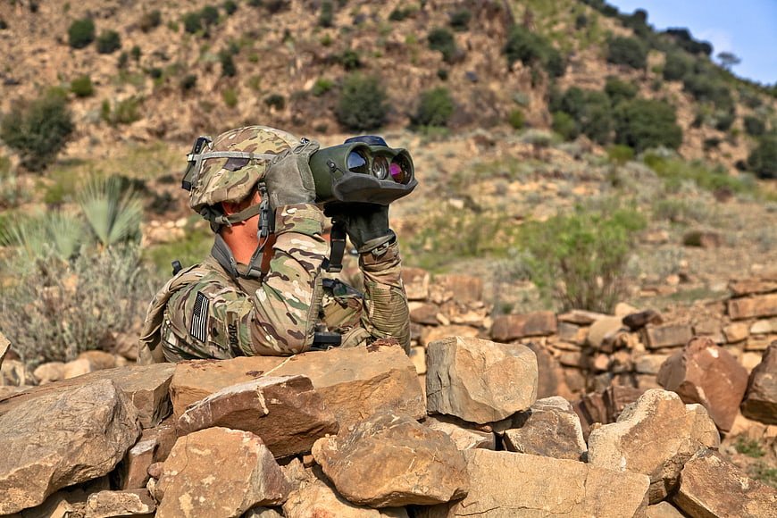 Soldier Using Binoculars Behind Rock Wall In Arid Landscape