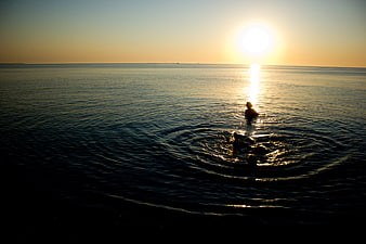 Silhouette of person swimming in ocean at sunset