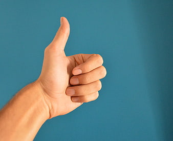 Hand Giving Thumbs Up Gesture Against Solid Blue Background