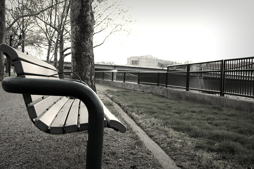 Empty park bench near river with city skyline background