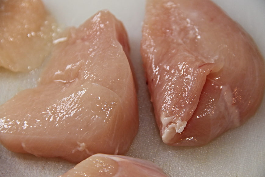 Raw chicken breasts on white cutting board