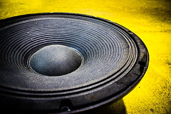Close-up of black speaker driver on textured yellow background