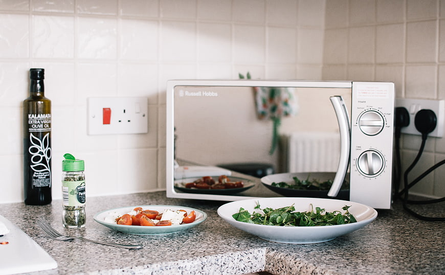 Healthy salad and ingredients on kitchen counter with microwave