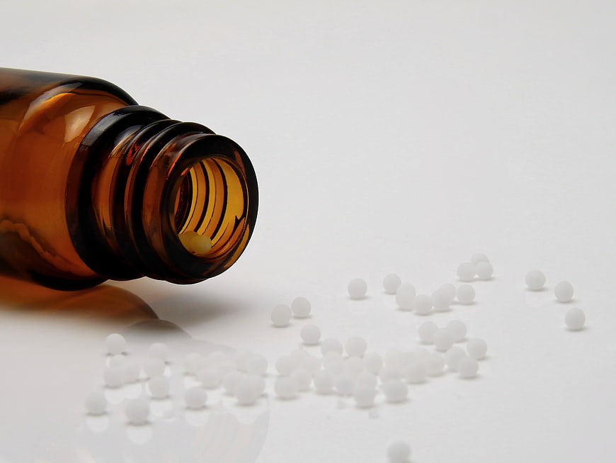 Amber glass vial with white homeopathic globules on white background