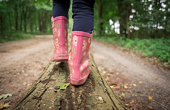 Child in pink floral rain boots walking on a log in a forest