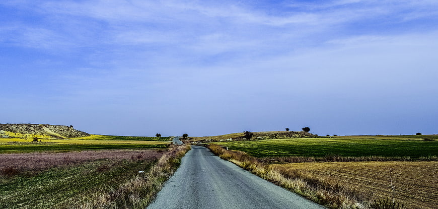 Paved road winding through green and yellow autumn fields in Cyprus