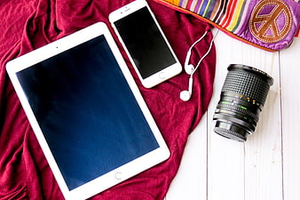 Flat lay of tablet, smartphone, camera lens, and headphones on red fabric