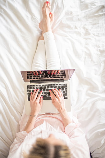 Woman typing on laptop in bed from top view