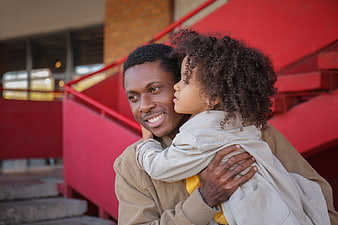 Happy Black Father Holding Young Daughter on Red Stairs