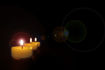 Three lit tea candles in a row with lens flare on black background