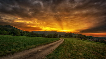 Dramatic sunset over rural road with sunbeams and green hills
