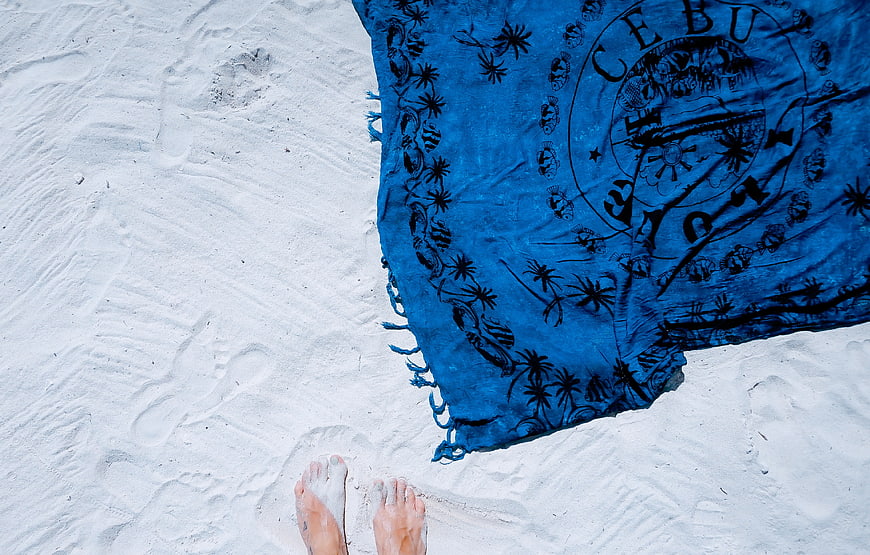 Top down view of feet on white sand with blue sarong