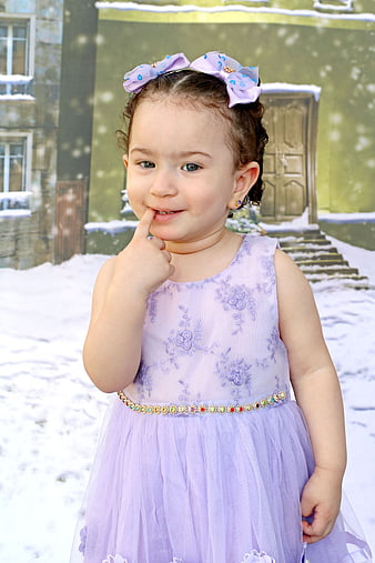 Cute toddler girl in purple dress posing in snow