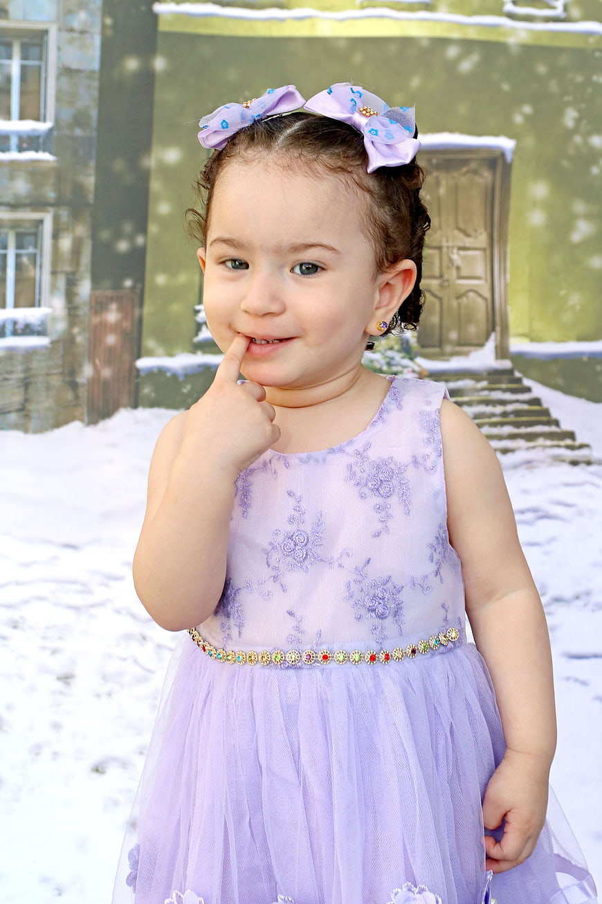 Cute toddler girl in purple dress posing in snow