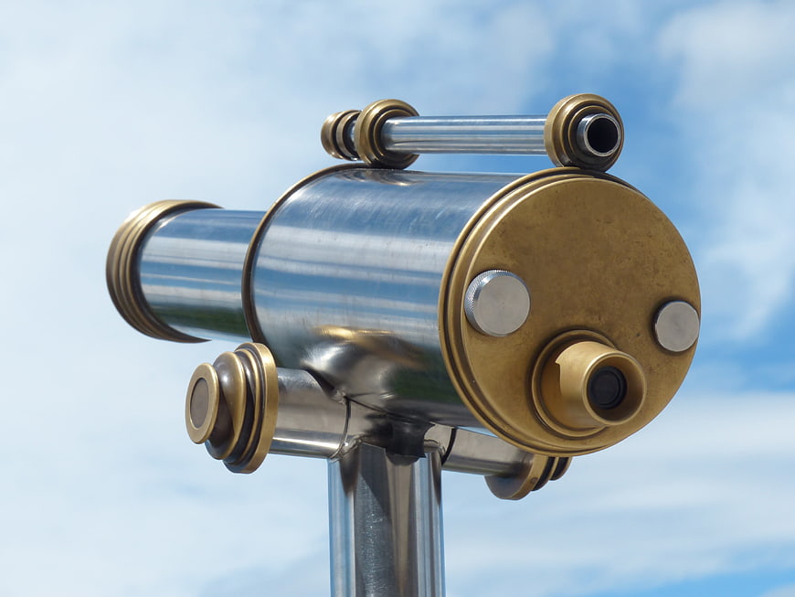 Close-up of brass and silver coin-operated telescope against blue sky