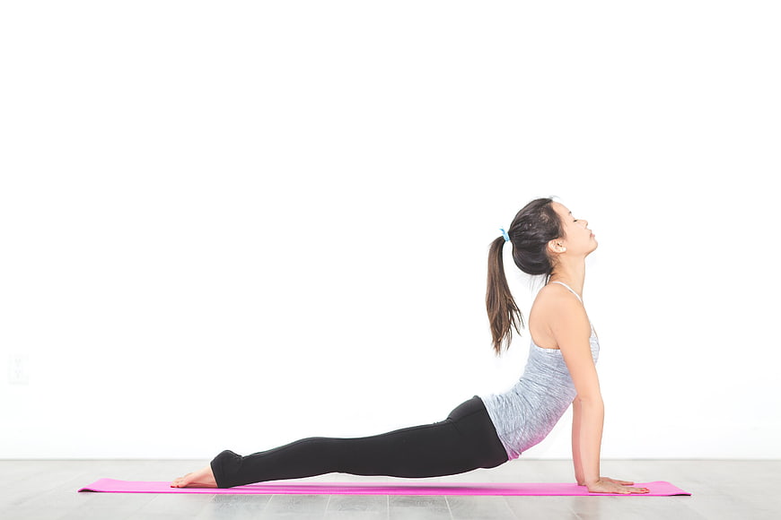 Woman performing cobra yoga pose on pink mat