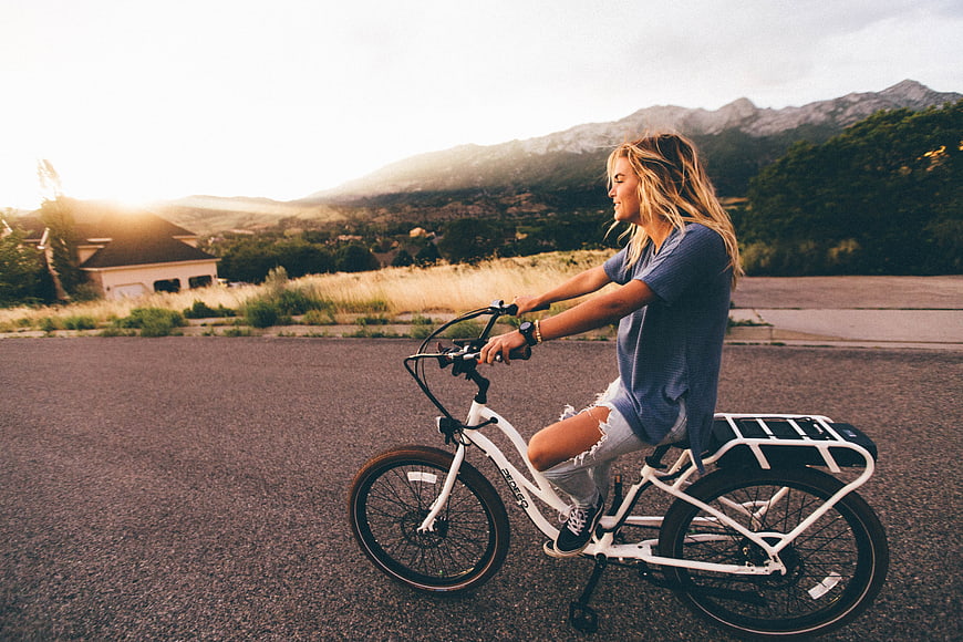 Woman riding white electric bike on road at sunset