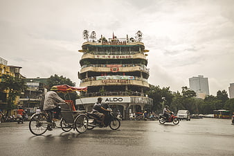 Cyclo and Motorbikes Crossing Hanoi Street Near Distinctive Round Building
