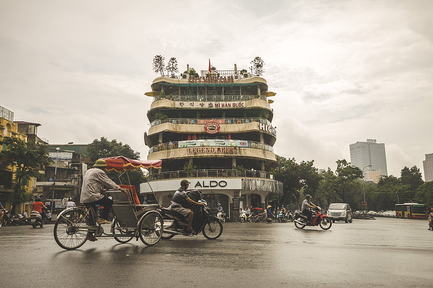 Cyclo and Motorbikes Crossing Hanoi Street Near Distinctive Round Building