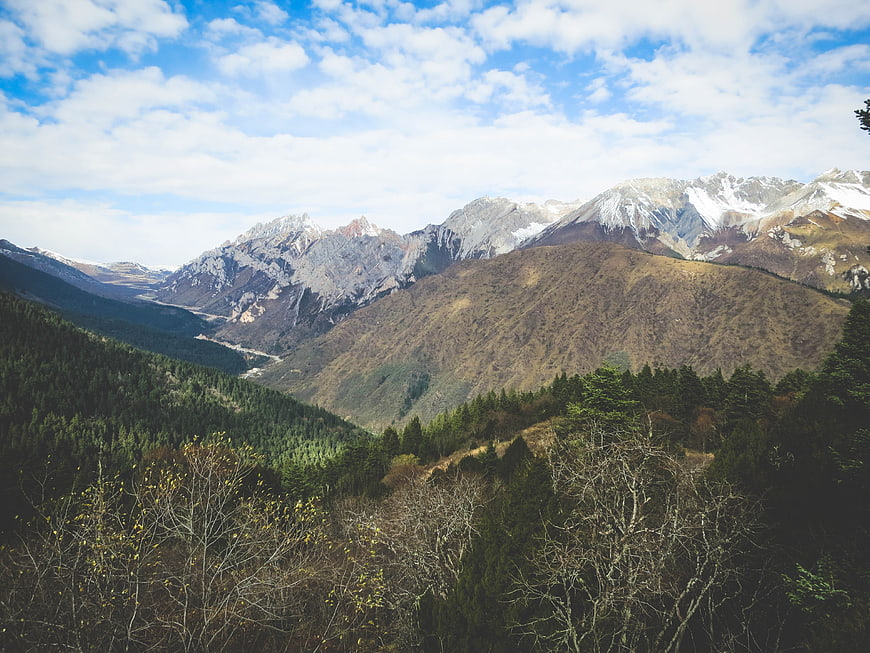 Snow-capped mountain range with forested valley and blue sky