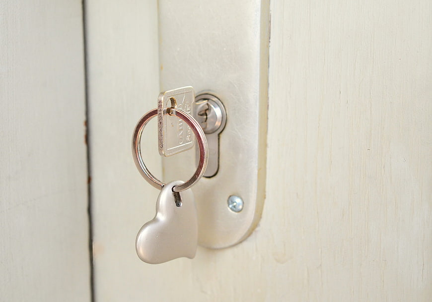 Silver key with heart charm in white door lock