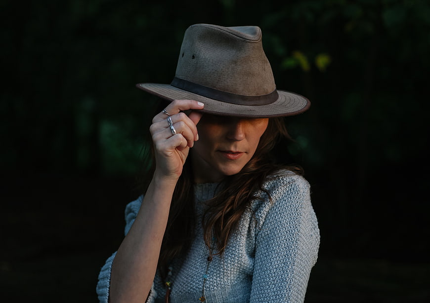 Woman in Fedora Hat Holding Brim in Dark Forest