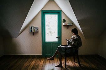 Woman relaxing in attic room reading phone with coffee