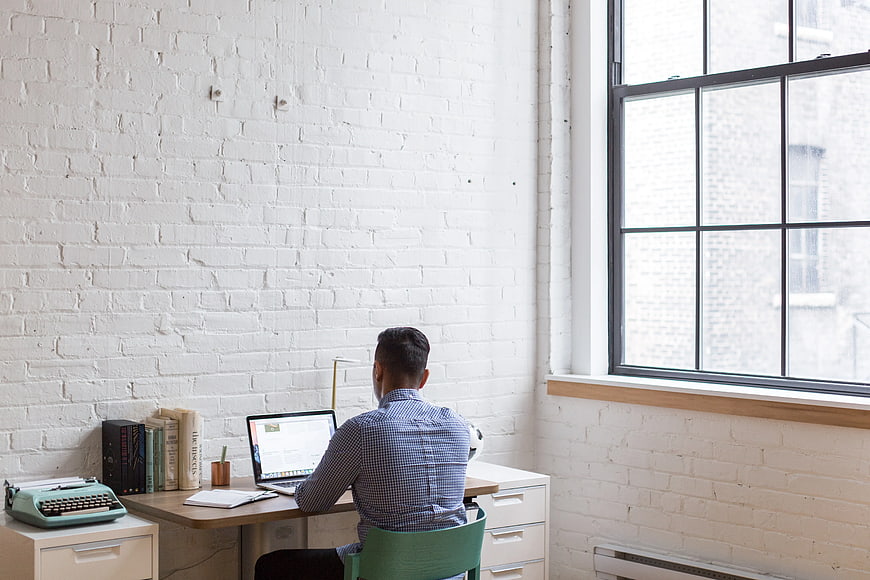 Man working on laptop in bright white brick office