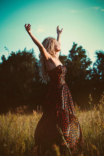 Blonde woman in polka dot dress celebrating freedom in field
