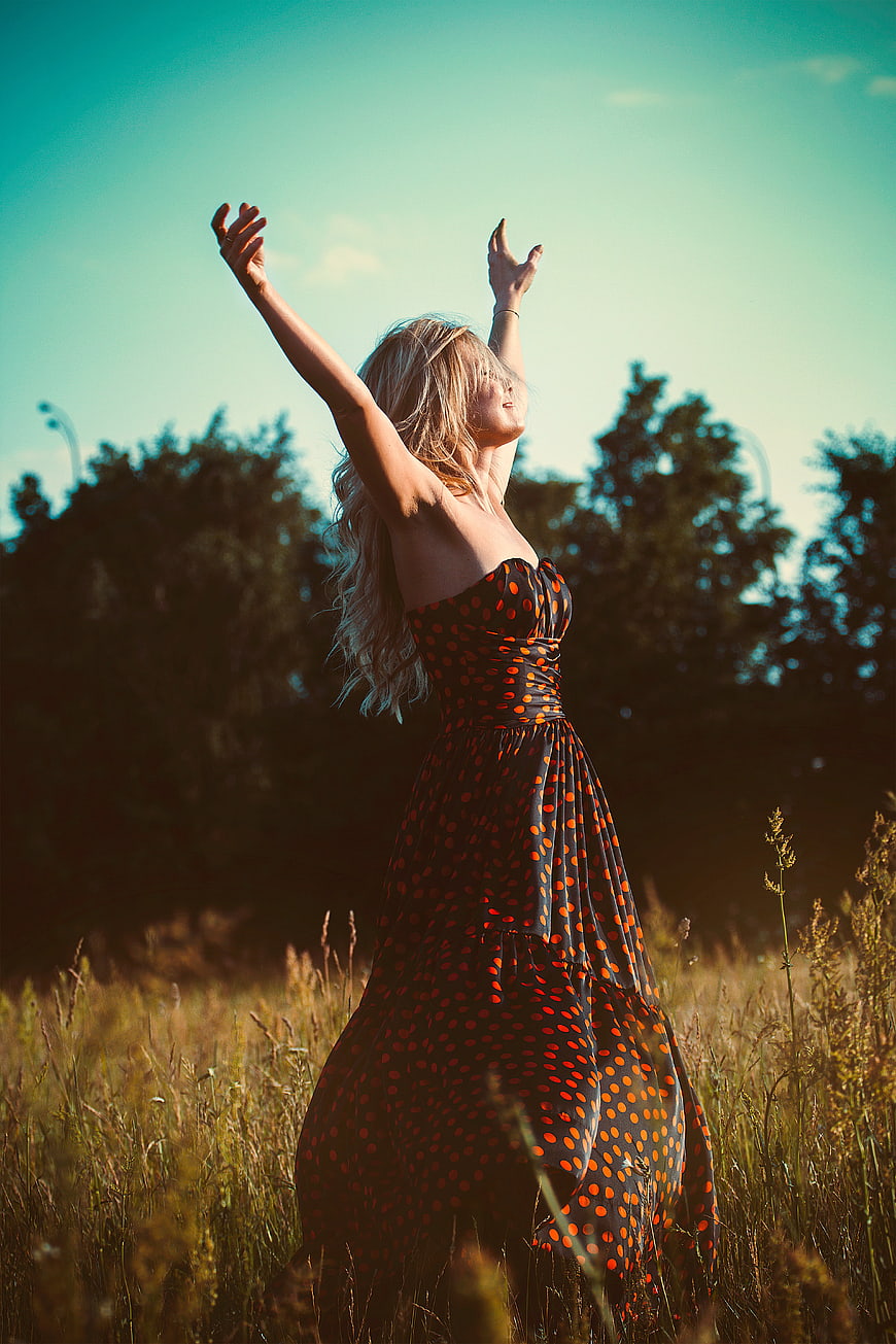 Blonde woman in polka dot dress celebrating freedom in field