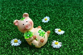 Cute ceramic pig figurine holding clover on green grass with daisies