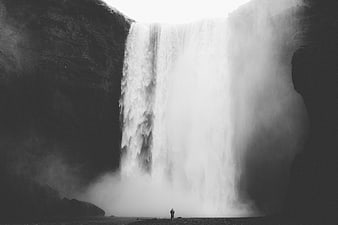 Black and white photo of a lone figure standing before a massive waterfall