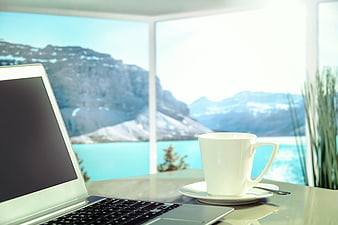 Laptop and coffee cup on table with mountain lake view