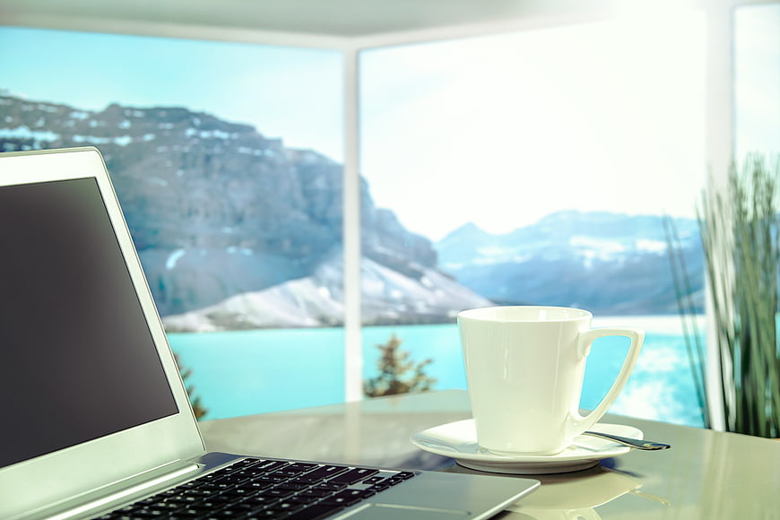 Laptop and coffee cup on table with mountain lake view