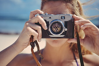 Woman holding vintage film camera on sunny beach