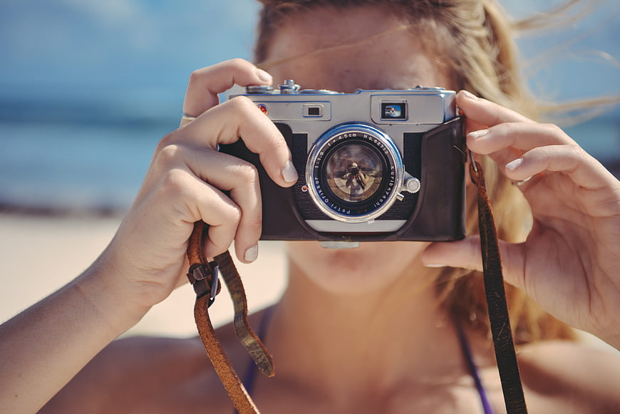 Woman holding vintage film camera on sunny beach