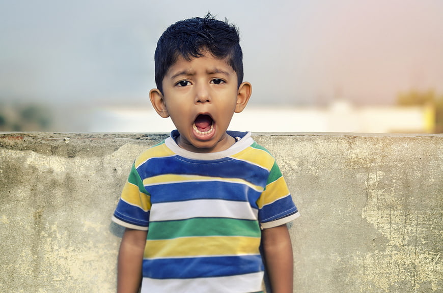 Young boy shouting with open mouth against concrete wall