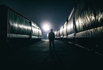 Silhouette of Man Standing Between Semi-Trucks at Night