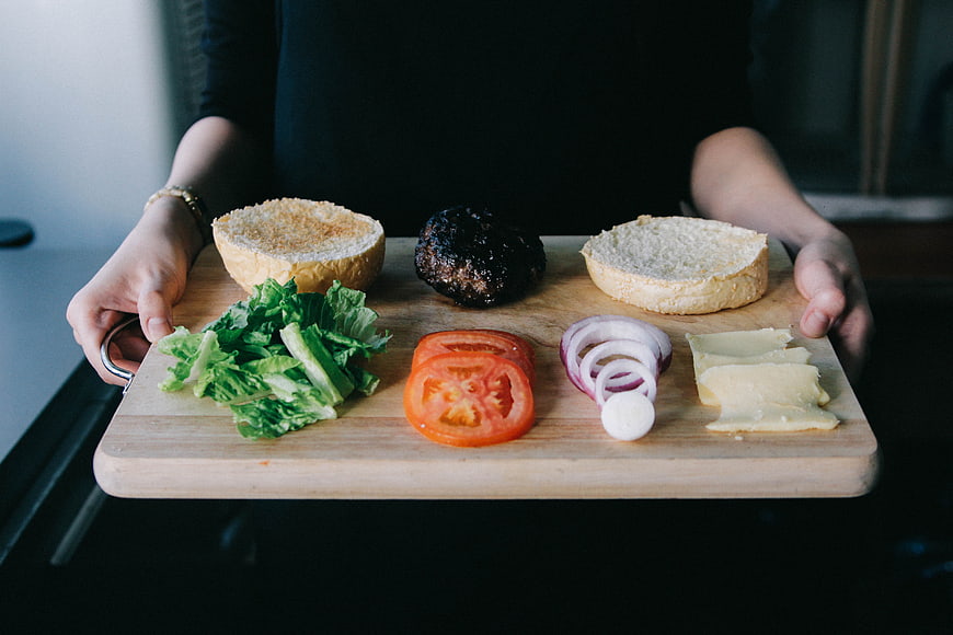 Hands holding wooden board with burger ingredients