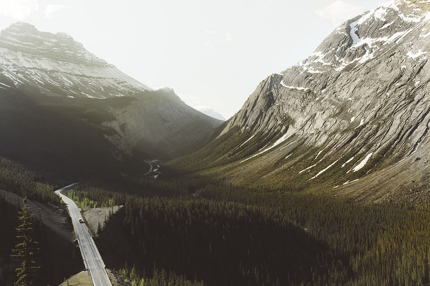 Winding mountain road through forested valley with snow-capped peaks