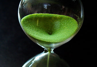 Close-up of green sand flowing through a glass hourglass