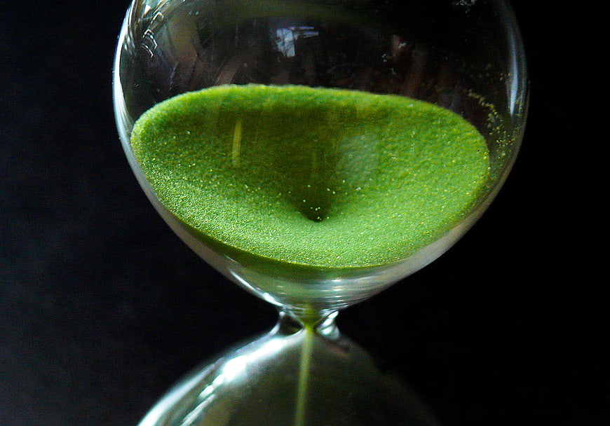 Close-up of green sand flowing through a glass hourglass